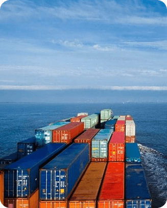 A cargo ship loaded with colorful shipping containers sails across a calm sea under a clear sky.